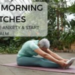 Woman seated cross-legged on a yoga mat in a softly lit morning room, gently stretching her neck with eyes closed—illustrating a calming morning stretch routine designed to reduce anxiety and promote mental clarity.